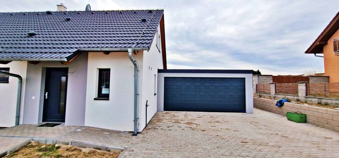 Prefabrikovaná garáž pre dve autá spojená s domom s hotovou omietkou, širokými dverami, dvoma oknami a dverami na zadnej stene